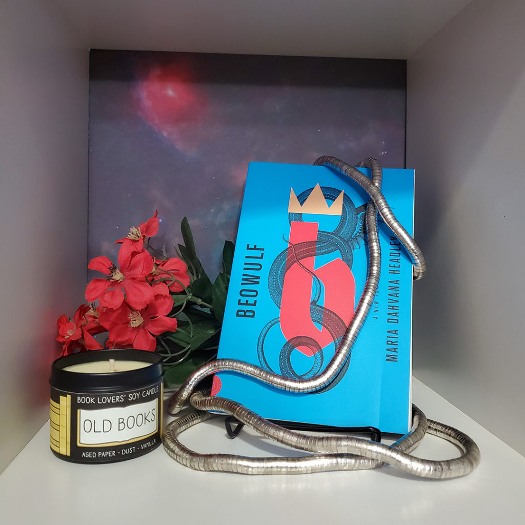 A photo of Beowulf: A New Translation with an old books-scented candle and some red flowers.