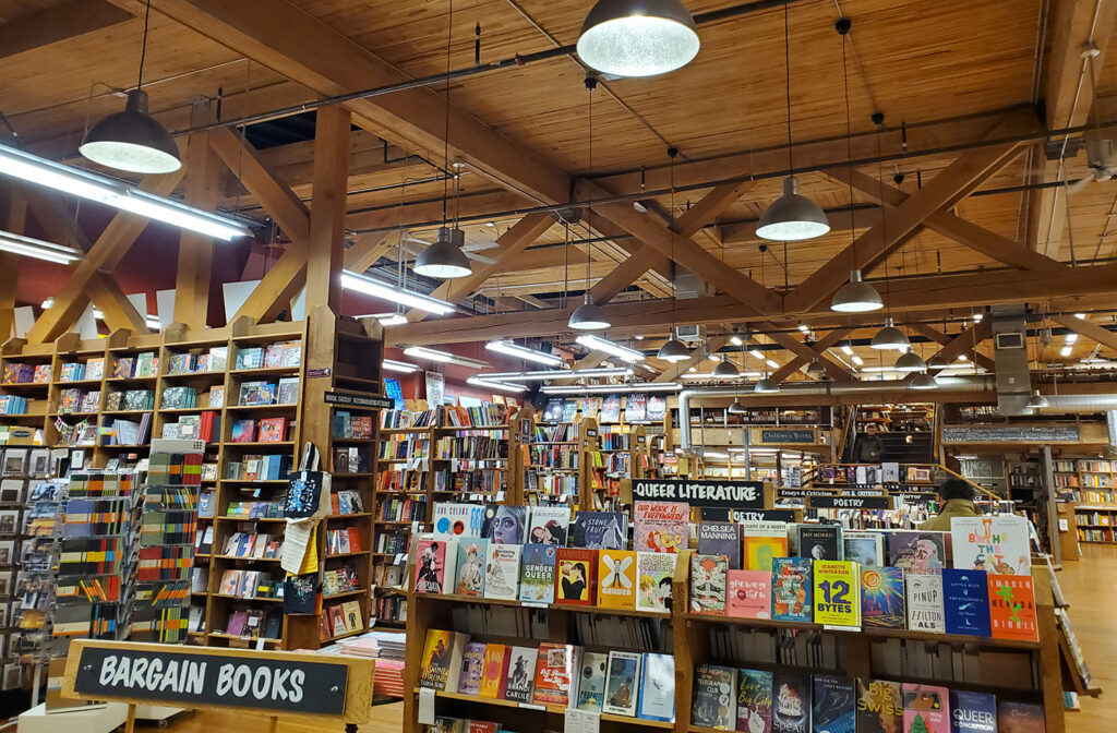 The queer literature section at Elliott Bay Books, that also shows a wider shot of the store behind it. It's a spacious, well-lit store.