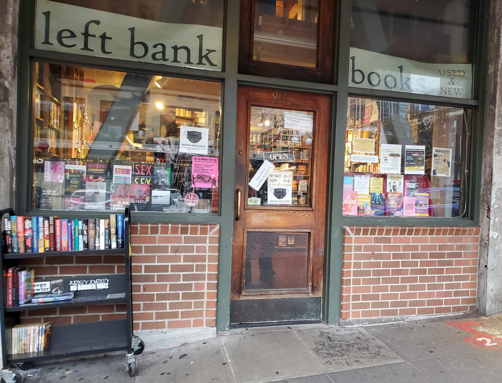 The storefront for Left Bank Books. It has a wooden door and windows full of books and flyers.