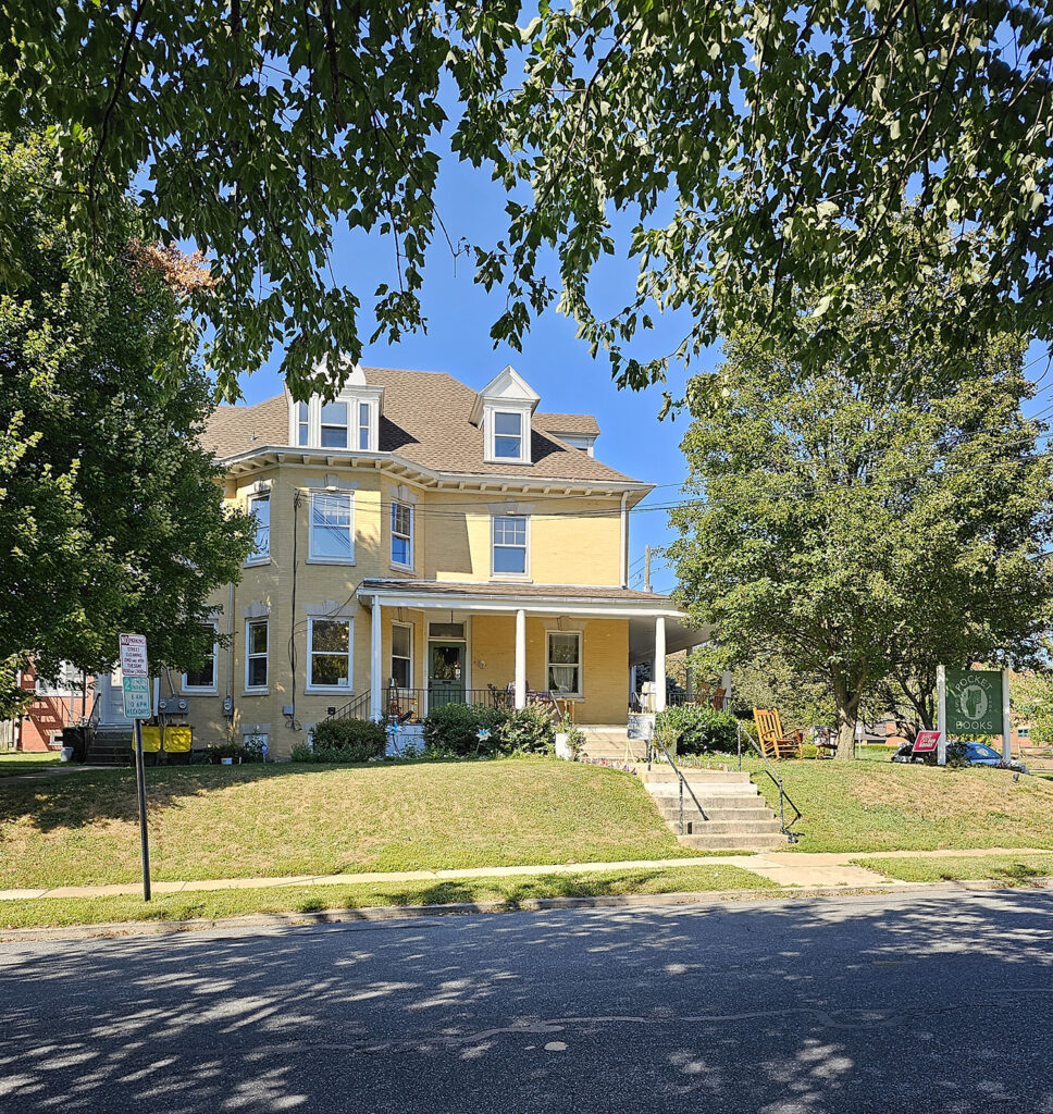 A shot of the exterior of Pocket Books. It's in an old yellow house and the walk way is lined with small pride flags.