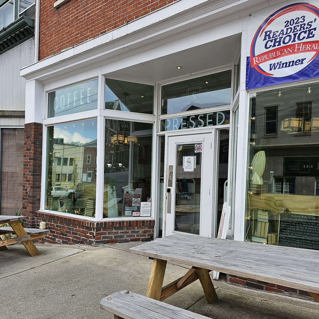 The storefront for Pressed Coffee and Books. There are wooden picnic tables out front.