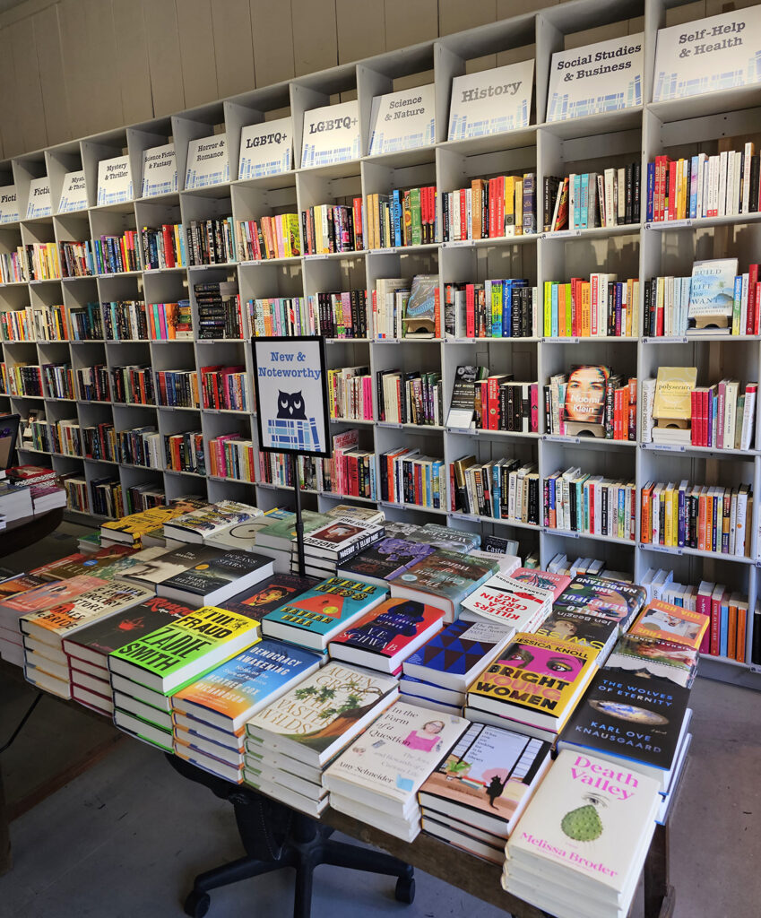 The inside of Provincetown Bookshop. The shelves are white and have large genre signs at the very top.